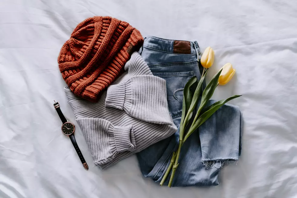 Gray shirt, light-wash jeans, an orange knitted beanie, and watch all laid on bed with two yellow tulips on top.